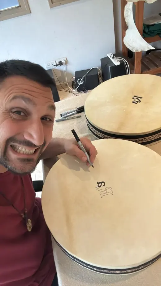 Ramiro Chaves sonriendo mientras escribe sobre el parche de un tambor en su taller