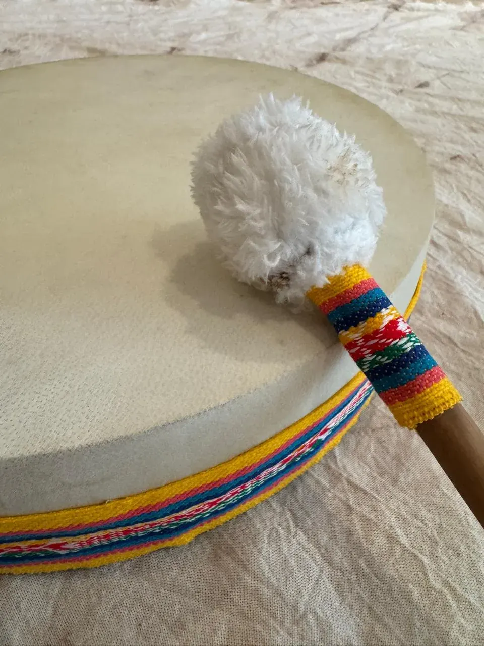 Tambor TUM con faja tejida de colores y su baqueta de lana sobre el parche